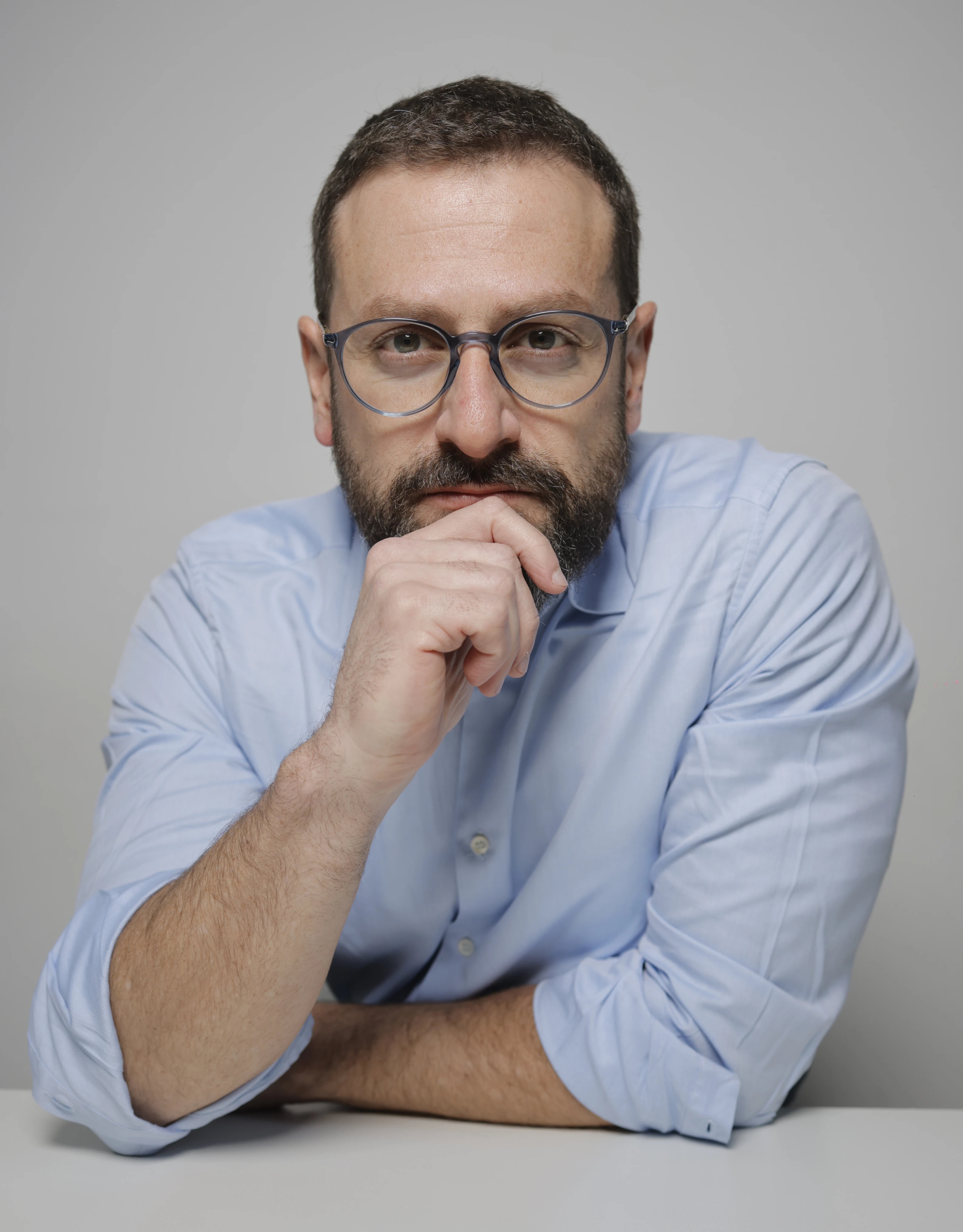 Foto do Dr. Italo Marsili, de camisa azul clara, óculos redondos e barba, apoiado sobre uma mesa